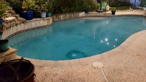 Ein Garten mit Schwimmbad, umgeben von Kübelpflanzen und einem Holzzaun.