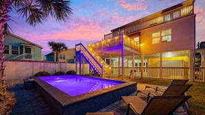 A swimming pool with a blue-lit deck, outdoor seating, and a multi-story building with balconies. - 5BR Beach House w/ Heated Pool | Great Views! (North Myrtle Beach)