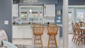 A kitchen with white cabinets, a bar area with wooden chairs, and a sign reading 'BEACH CHERRY GROVE'. - 5BR Beach House w/ Heated Pool | Great Views! (North Myrtle Beach)