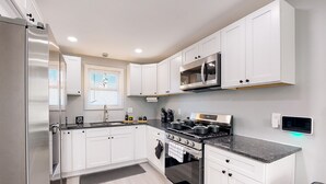 Una cucina moderna con mobili bianchi, un frigorifero in acciaio inox, un forno a microonde e un piano cottura a gas.