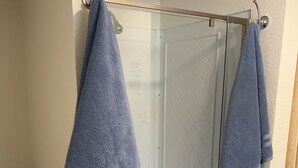 Ett badrum med en duschkabin med glasväggar, en toalett och två handdukar som hänger på krokar.