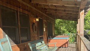 A wooden porch with two rocking chairs, a red bench, and a view of trees.