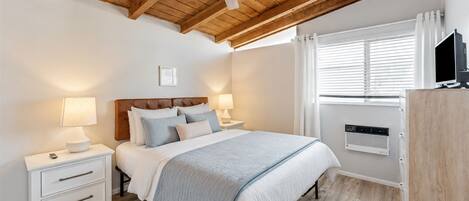 Un dormitorio con cama, mesitas de noche, ventilador de techo, ventana con persianas y televisión empotrada.