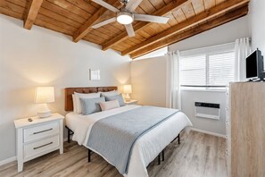 A bedroom with a bed, nightstands, a ceiling fan, a window with blinds, and a built-in TV. - Cozy Beach View Loft, 42 Steps to the Sand + AC (Ventura)