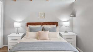 Une chambre à coucher avec un lit, des tables de chevet, des lampes et un tableau accroché au mur.
