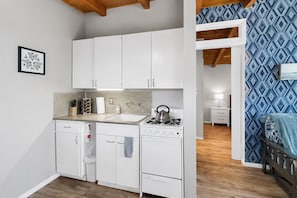 Une cuisine compacte avec des meubles blancs, une cuisinière à gaz, un évier et un petit plan de travail.
