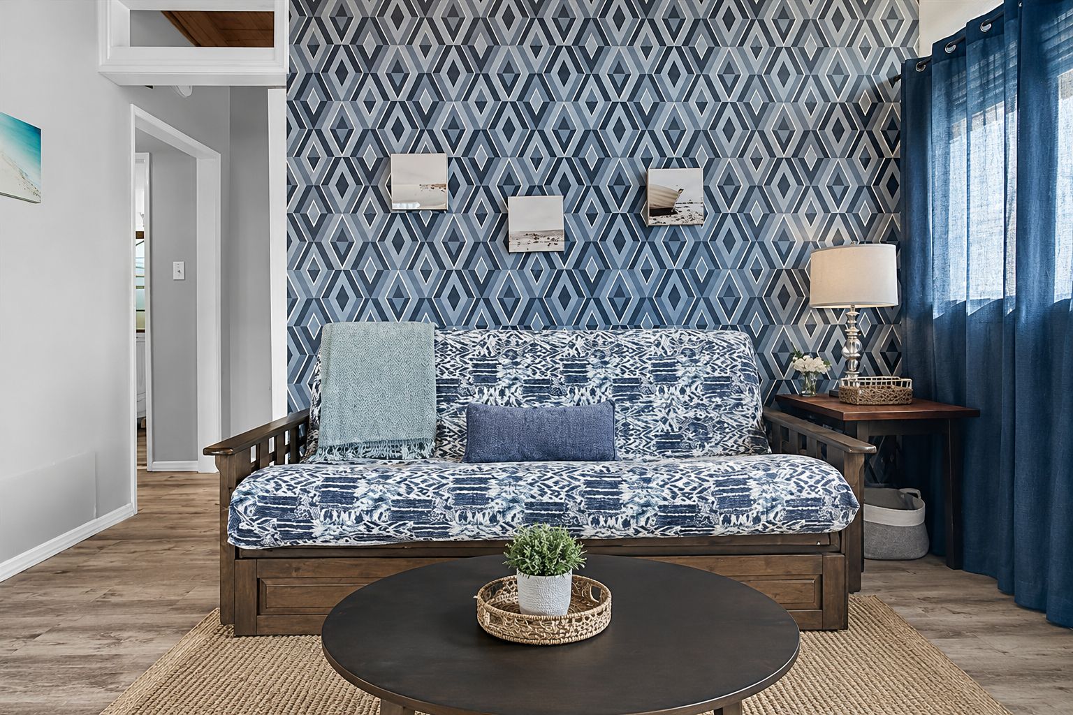 A cozy living room with a patterned sofa, a small table with a plant, and a wall with geometric wallpaper.