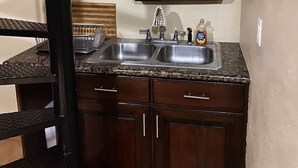 A kitchen with a double sink, dark wooden cabinets, a decorative metal backsplash, and a small shelf with a vase of flowers. - Sunset Loft (Nassau)