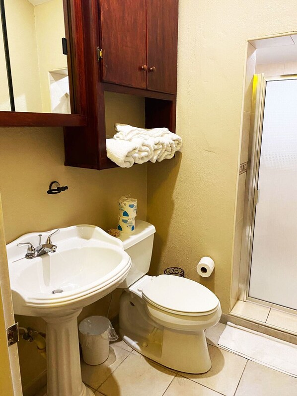 A bathroom with a pedestal sink, toilet, and a wooden cabinet above the toilet.