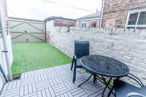 Une terrasse avec une table et des chaises, un mur en briques et une zone herbeuse.