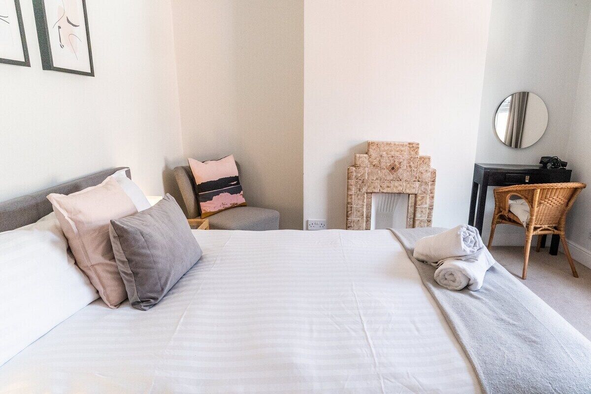 A hotel room with a large bed, a chair, a small table, and a mirror on the wall.