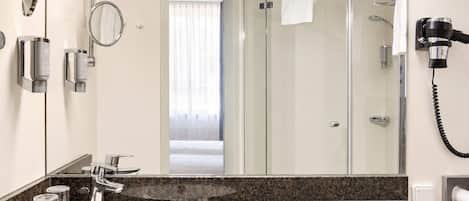 Un baño moderno con lavamanos de mármol, cabezal de ducha de mano, secador de pelo y mampara de vidrio.