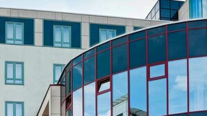 A modern building with a curved glass facade and multiple windows. - Rugs Hotel Augsburg, Trademark Collection by Wyndham (Augsburg)