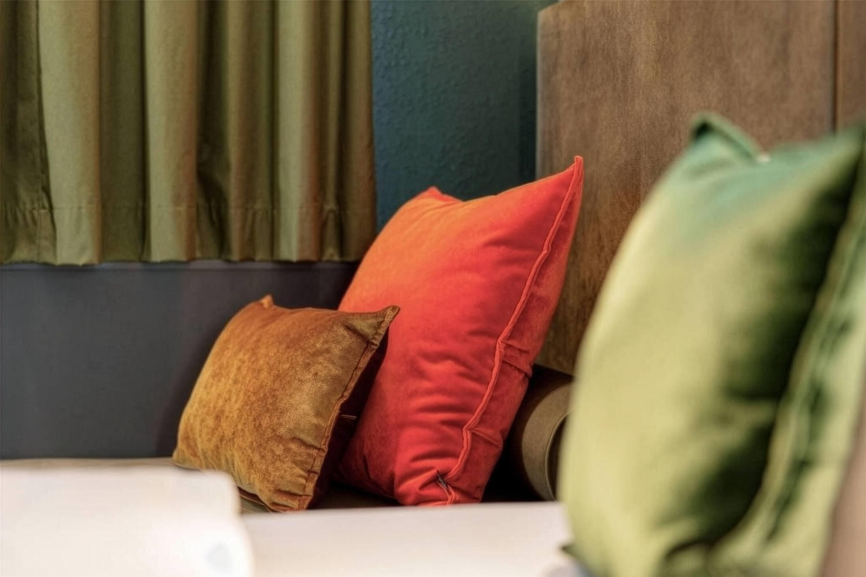 A room with a sofa and three pillows in different colors.
