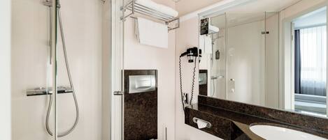 Un baño moderno con cabina de ducha de vidrio, inodoro blanco, encimera de mármol y un espejo grande.