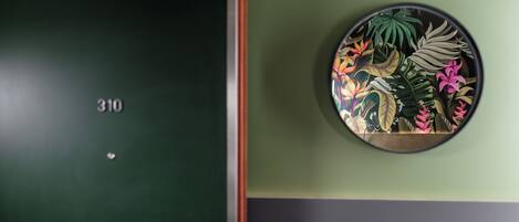 Una puerta con el número 310, una pared verde y un adorno circular con hojas y flores tropicales.