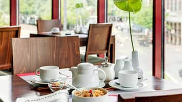 A dining table with white ceramic tableware, a bowl of cereal, and a newspaper.