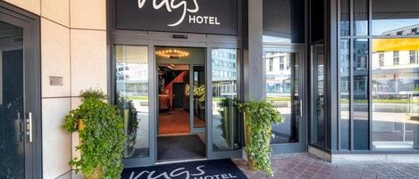 La entrada del Hotel Rugs, con un toldo negro, puertas de vidrio y un felpudo.