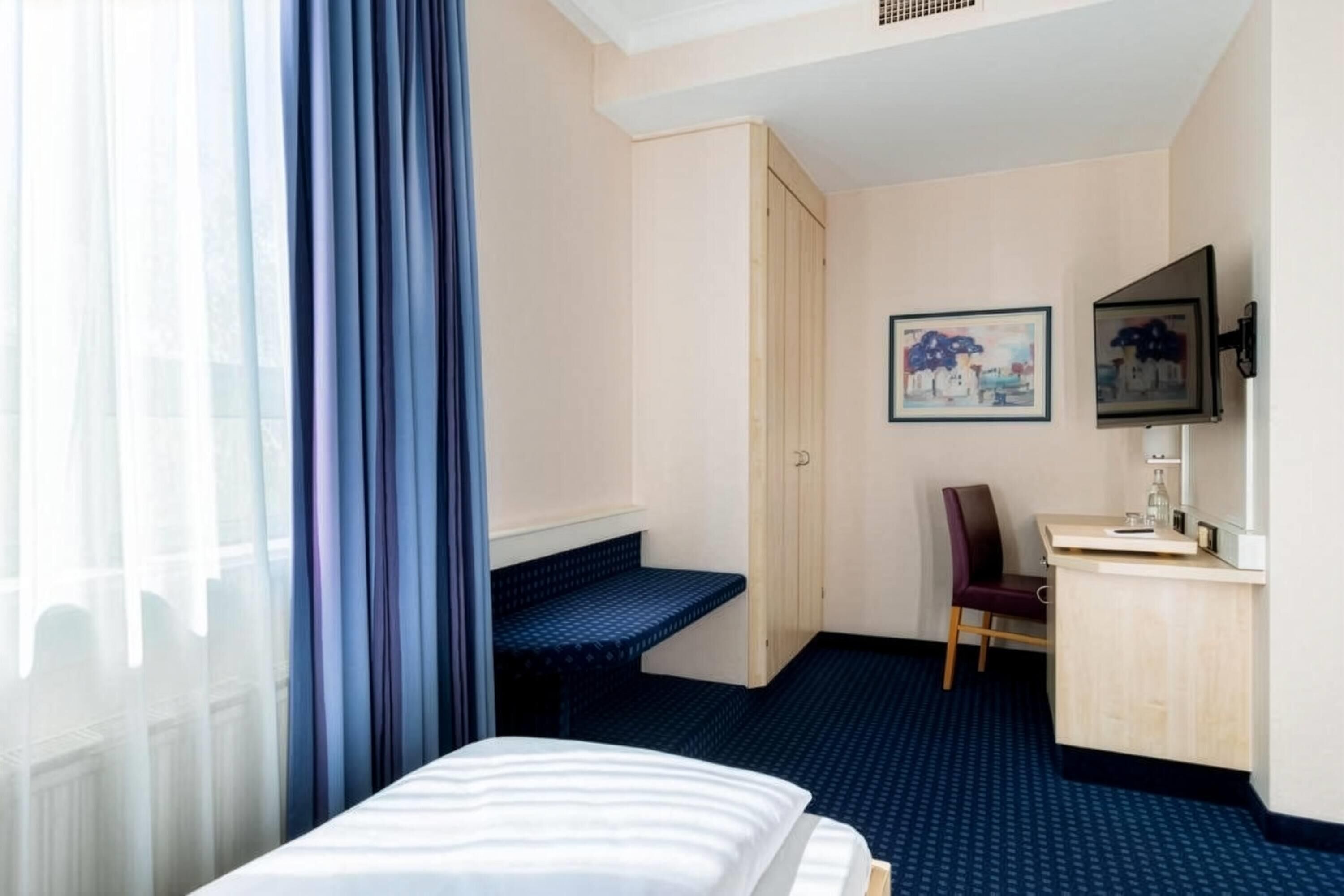 A hotel room with a bed, a desk, a chair, and a window with curtains.