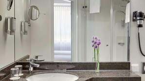 A modern bathroom with a large mirror, a sink, and a shower. There are toiletries on the counter and a hairdryer on the wall. - Rugs Hotel Augsburg, Trademark Collection by Wyndham (Augsburg)