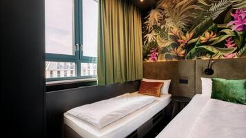 A hotel room with a bed, a window with curtains, a headboard with a floral mural, and a view of buildings outside.