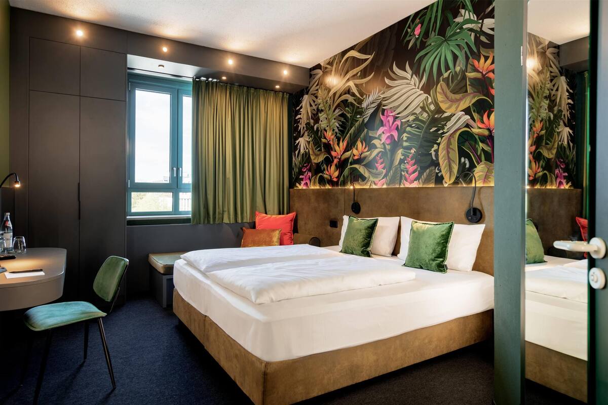 A hotel room with a large bed, a desk, a chair, and a window with curtains.