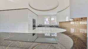 A modern kitchen with white cabinetry, a central island, and a curved marble floor. - QUAINT HIGH-FLOOR RETREAT ON QUAI D'ORSAY – EMBRACE THE PARISIAN LIFESTYLE (Paris)