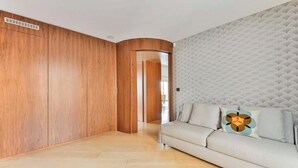 A modern living room with a light-colored sofa, a decorative pillow, and a textured wall. - QUAINT HIGH-FLOOR RETREAT ON QUAI D'ORSAY – EMBRACE THE PARISIAN LIFESTYLE (Paris)