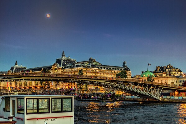 A historic building with a prominent clock tower, a green dome, and a bridge with people walking across it.