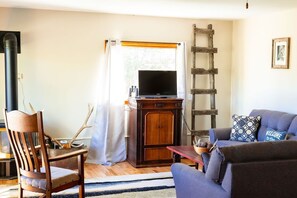 Ein Wohnzimmer mit einem Holzstuhl, einer Couch, einem Fernseher auf einem Schrank und einer an der Wand stehenden Leiter.