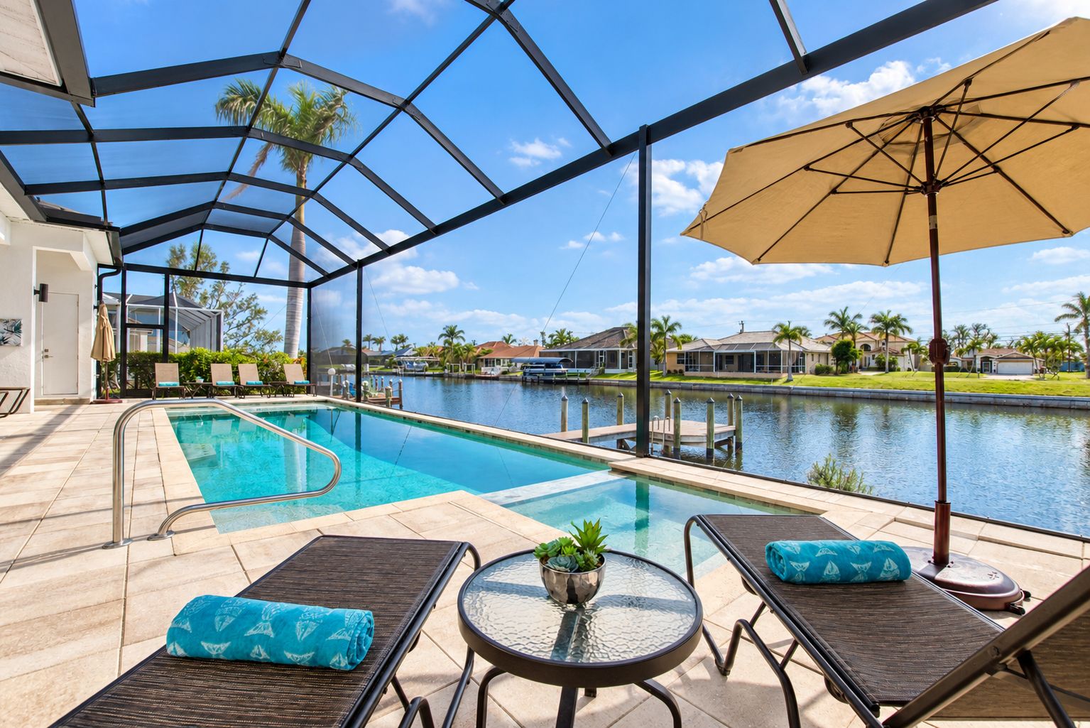 A pool area with lounge chairs and a table, overlooking a body of water and residential buildings.