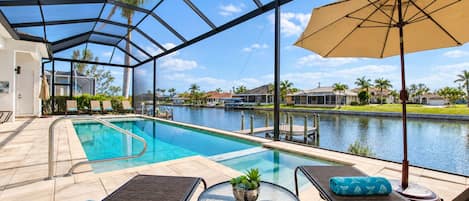 A pool area with lounge chairs and a table, overlooking a body of water and residential buildings.