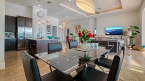 Una cocina moderna con una isla central, comedor con sillas y una lámpara de araña grande.