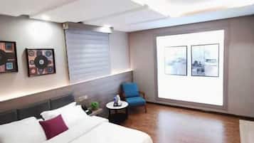 A hotel room with a bed, a blue armchair, a small table, and two framed pictures on the wall.