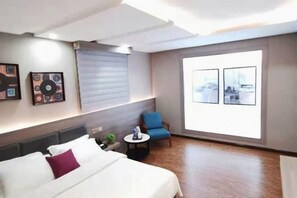 A hotel room with a bed, a blue armchair, a small table, and two framed pictures on the wall. - Hongrui Hotel (Anlong)