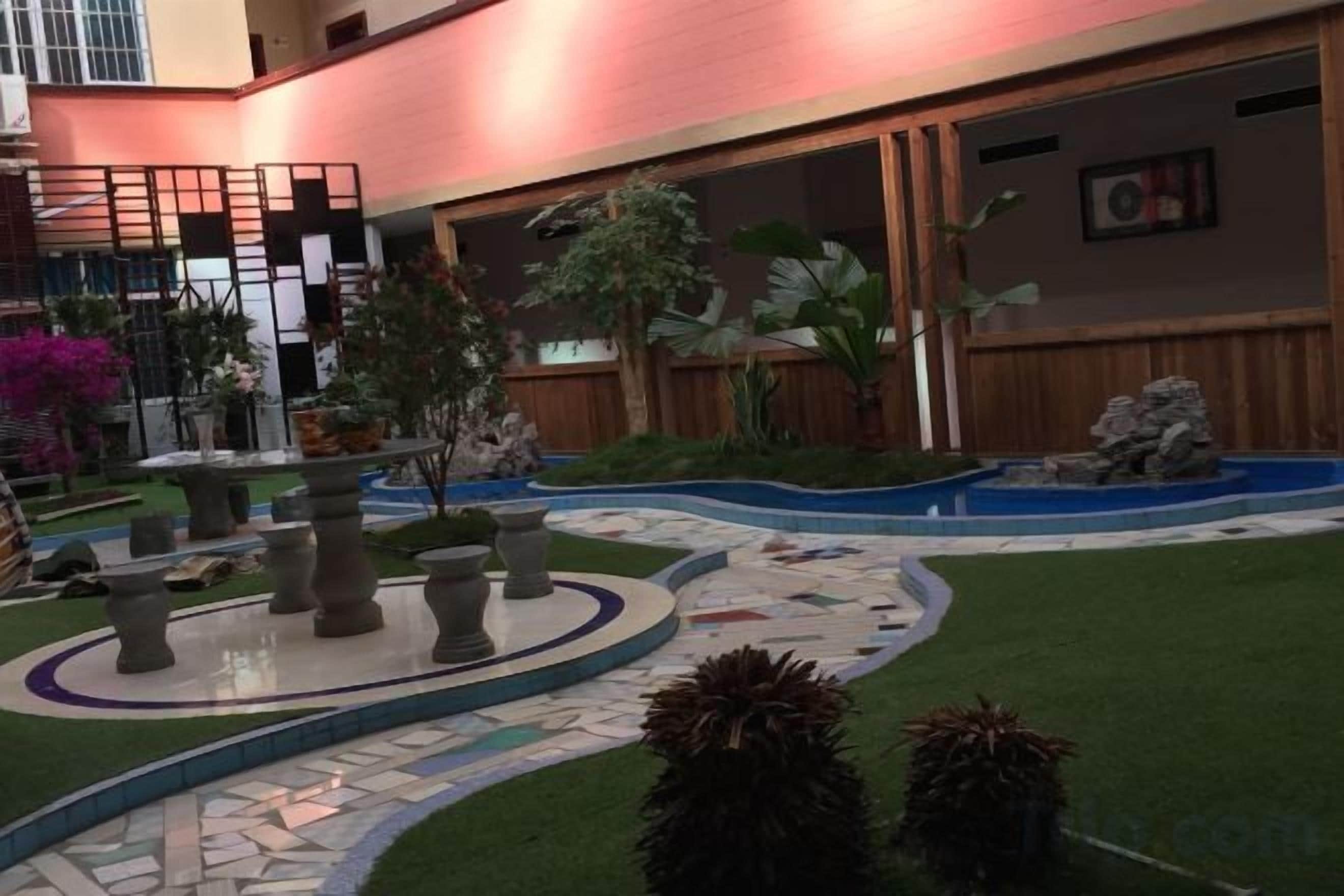 Un patio con una fuente, plantas en macetas y un sendero empedrado.