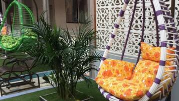 A hanging chair with a floral pattern, a green chair, and a potted plant in a garden area.