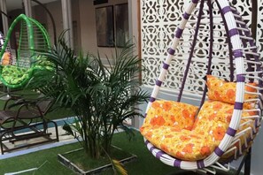 A hanging chair with a floral pattern, a green chair, and a potted plant in a garden area. - Hongrui Hotel (Anlong)