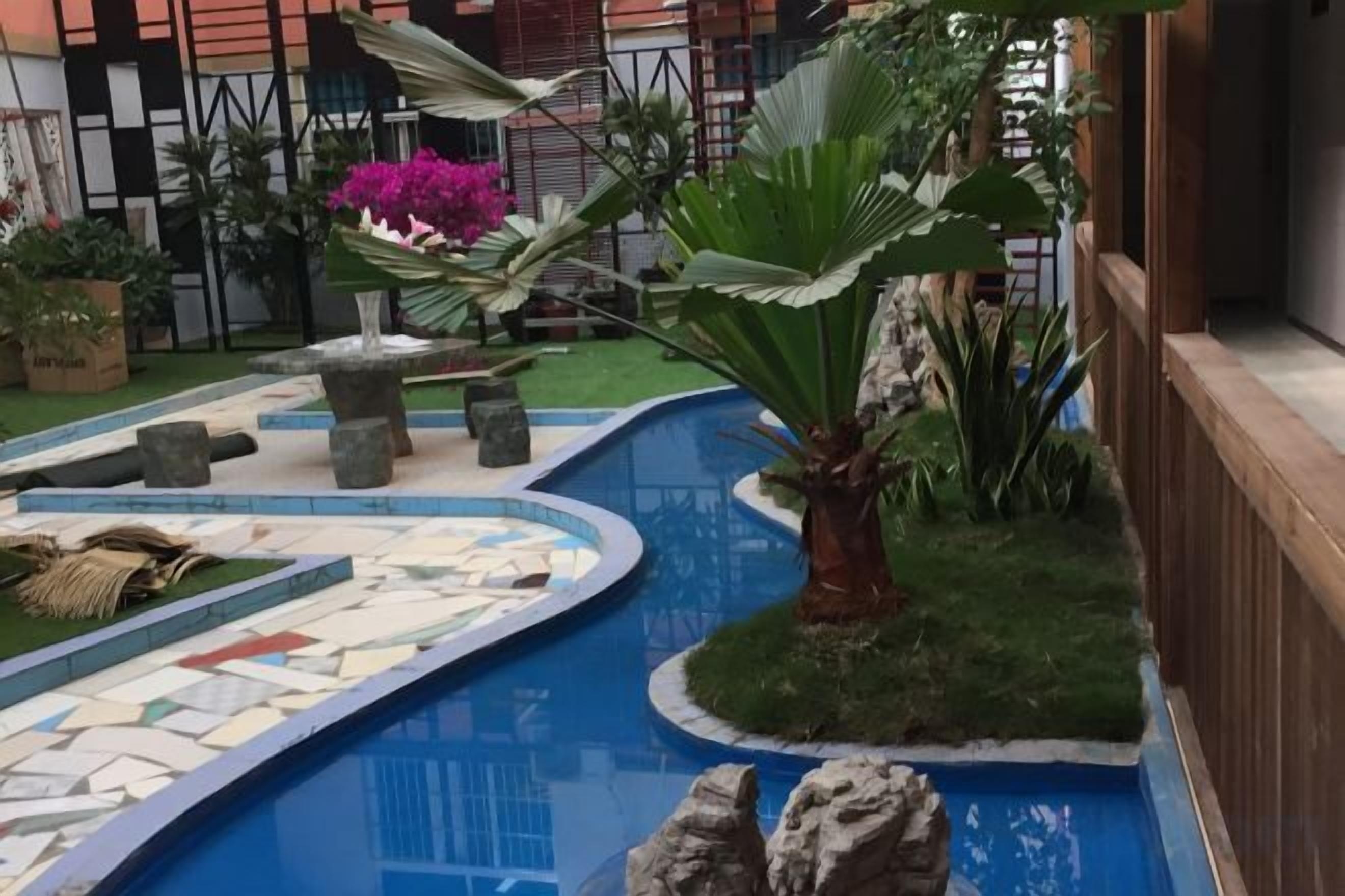 A swimming pool with a tiled edge, surrounded by greenery and a wooden fence.