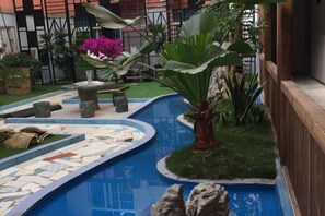 Una piscina con borde de azulejos, rodeada de vegetación y una valla de madera.