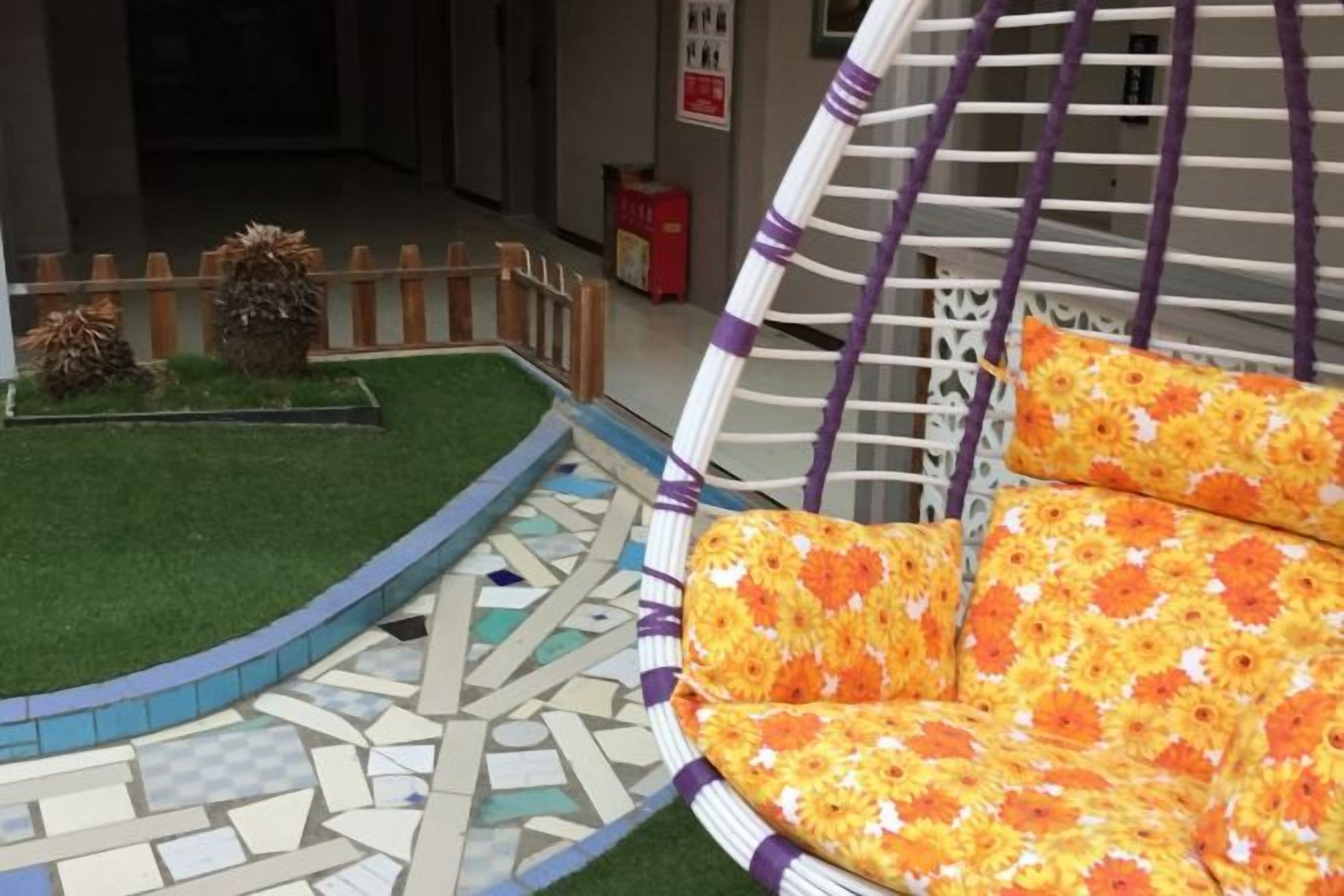 A wicker chair with floral cushions, a mosaic floor, and a small garden with a wooden fence.