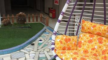 A wicker chair with floral cushions, a mosaic floor, and a small garden with a wooden fence.