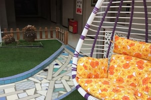 Una silla de mimbre con cojines estampados, un suelo de mosaico y un pequeño jardín con cerca de madera.