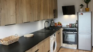 Une cuisine moderne avec des meubles en bois, un plan de travail noir, un lave-linge, un réfrigérateur et une plante en pot.