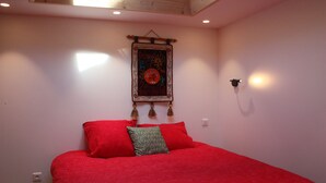 Une chambre avec un grand lit, une tapisserie murale et un luminaire fixé au mur.