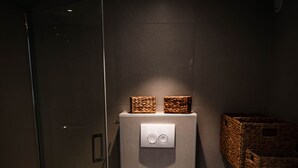 Une salle de bain moderne avec une douche à parois de verre, des toilettes blanches et une petite poubelle.