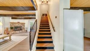 A staircase leading to a second floor with a stone fireplace and a modern light fixture above it.