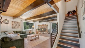 A modern living room with a fireplace, green sofas, and a staircase.