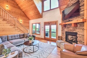 A spacious living room with a wooden staircase, a fireplace, and a large TV mounted on a stone wall. - 45 minutes to lake point! (Ranger)