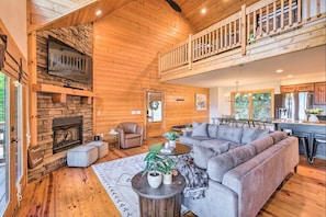 A spacious living area with a stone fireplace, wooden ceiling, and a balcony.